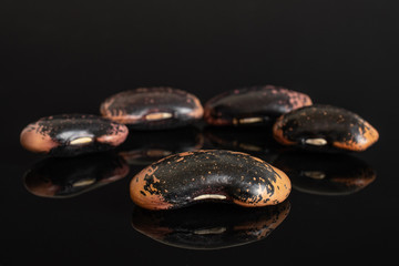 Group of five whole stained purple bean isolated on black glass