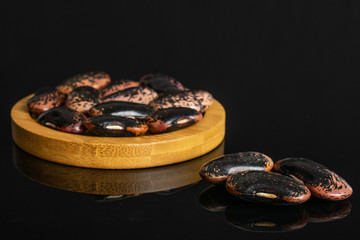 Lot of whole stained purple bean on round bamboo coaster isolated on black glass