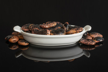 Lot of whole stained purple bean in white oval ceramic bowl isolated on black glass