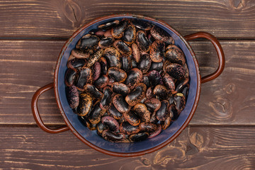 Lot of whole stained purple bean in old pot flatlay on brown wood