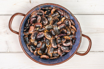 Lot of whole stained purple bean in old pot flatlay on white wood
