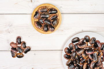 Lot of whole stained purple bean on round bamboo coaster on white ceramic plate flatlay on white wood