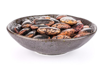 Lot of whole stained purple bean in dark ceramic bowl isolated on white background