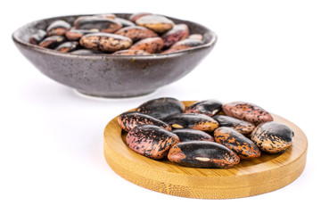 Lot of whole stained purple bean on round bamboo coaster in dark ceramic bowl isolated on white background