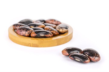 Lot of whole stained purple bean on round bamboo coaster isolated on white background