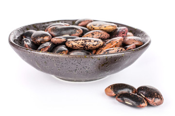 Lot of whole stained purple bean in dark ceramic bowl isolated on white background