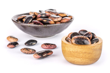 Lot of whole stained purple bean in dark ceramic bowl in tiny wooden bowl isolated on white background