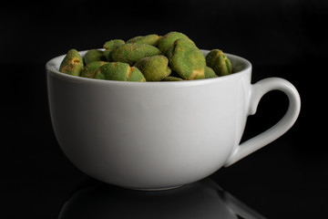 Lot of whole spicy green wasabi peanut in white ceramic cup isolated on black glass