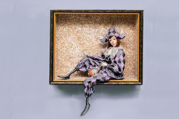 Doll in a harlequin costume in a frame