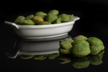 Lot of whole spicy green wasabi peanut small group is in the front and the rest is isolated on black glass