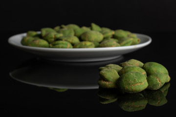 Lot of whole spicy green wasabi peanut small group is in the front and the rest is on white ceramic plate isolated on black glass