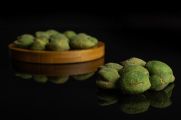 Lot of whole spicy green wasabi peanut small group is in the front and the rest is on bamboo coaster isolated on black glass