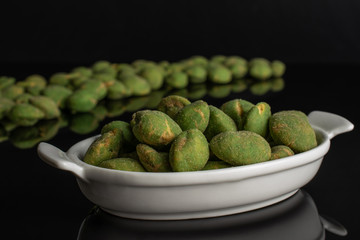 Lot of whole spicy green wasabi peanut large group is in the back and small group is in the front isolated on black glass