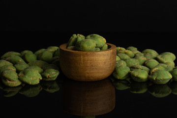 Lot of whole spicy green wasabi peanut in tiny wooden bowl isolated on black glass