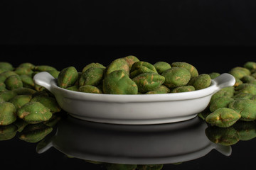 Lot of whole spicy green wasabi peanut in white oval ceramic bowl isolated on black glass