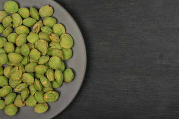 Lot of whole spicy green wasabi peanut on gray ceramic plate flatlay on grey stone