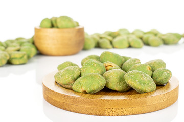 Lot of whole spicy green wasabi peanut on bamboo coaster in tiny wooden bowl isolated on white background
