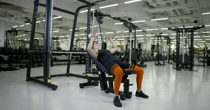 Sporty girl in the gym doing sitting leaning back exercise with dumbbells in hand, then zamanivaet and puts gandeli on the floor.