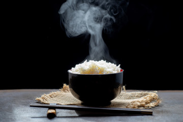 Cooked rice with steam in black bowl on dark background,hot cooked rice in bowl selective focus,hot food and healthy