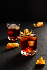 Negroni alcoholic cocktail in two glasses decorated with orange peel with ice cubes on a dark table