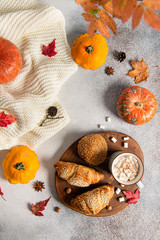 Autumn flat lay composition. Mug of hot cocoa, croissant, pumpkins and autumn leaves on grey background. Cozy autumn concept.