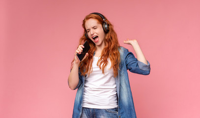 Emotional redhead girl singing into smartphone like microphone