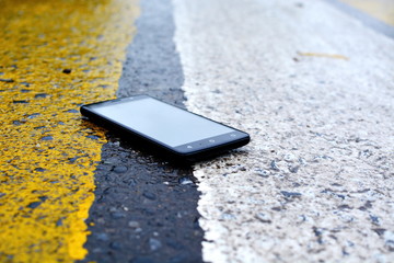 Fallen on road black smartphone lies on the asphalt surface wet from the autumn rain between the yellow and white lanes of the pedestrian crossing of street