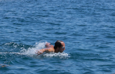 Homme nageant la nage papillon en pleine mer, tête sortie de l'eau pour reprendre son souffle