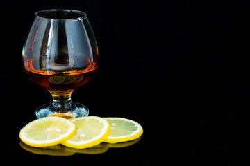 Glass of cognac and lemon slices isolated on black background. Copy space.