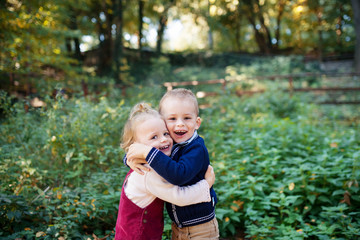 Fototapeta premium Twin toddler sibling boy and girl standing in autumn forest, hugging.
