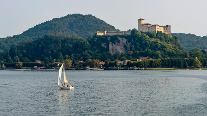 Wonderful view of the Rocca di Angera with a white sailboat sailing on Lake Maggiore, Italy nearby