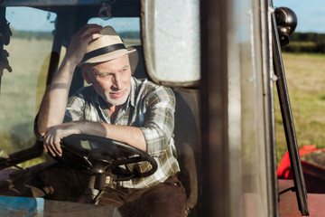 Fototapeta na wymiar selective focus of senior farmer touching straw hat while driving tractor