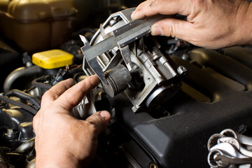 Hands measure the piston of a car engine using a ruler