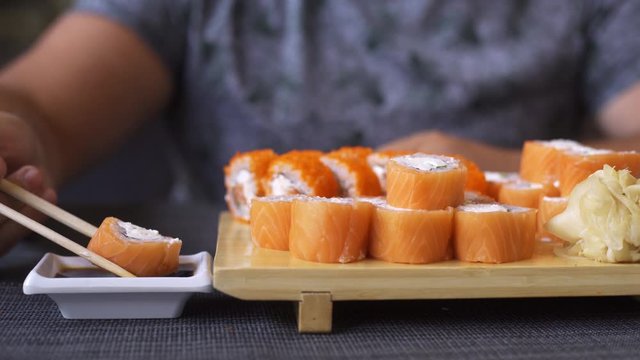 Pleasant chubby man with a beard in a sushi bar, eating rolls. Does not know how to handle sticks, rolls fall out.
