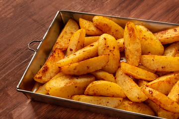 Potato wedges, oven roasted, in a vintage baking tray on a dark rustic wooden background