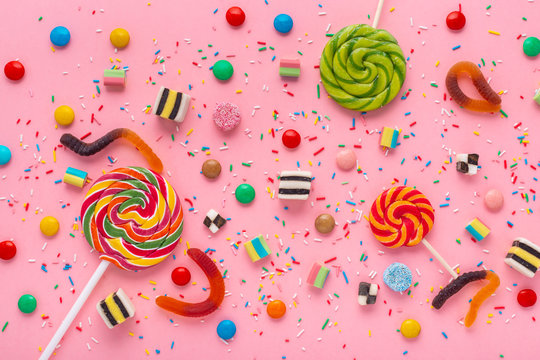 flat lay of candies festive background with assortment of colourful caramel with jelly and sprinkles over pink