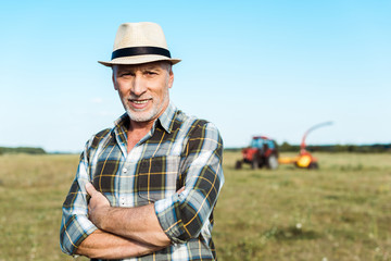 Naklejka na ściany i meble happy senior farmer standing with crossed arms in field