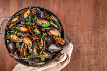 Marinara mussels, moules mariniere, in a large cooking pan, overhead shot on a dark rustic wooden background