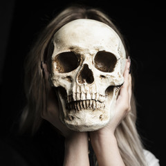 Woman holding human skull with black background