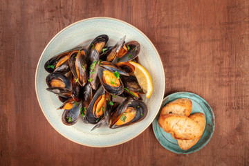 Marinara mussels, moules mariniere, overhead shot on a dark rustic wooden background with toasted bread and copyspace