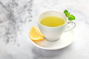 A cup of tea with a slice of lemon and mint leaves, with an organic plant shadow and copy space