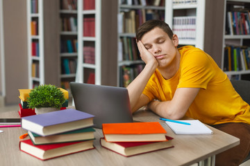 Male student sleeping at workplace in college library