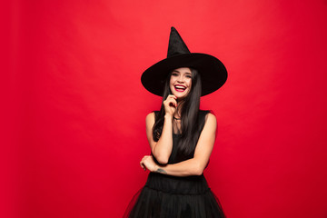 Young brunette woman in black hat and costume on red background. Attractive caucasian female model....