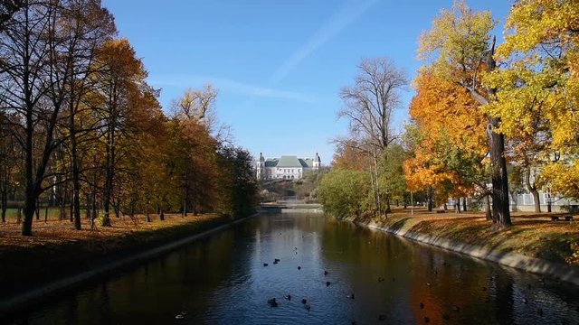 City park Royal Lazienki with pond or lake and  Ujazdowski Castle on background with blue sky, trees and fallen leaves at autumn. Warsaw, Poland, Europe. Middle distance view