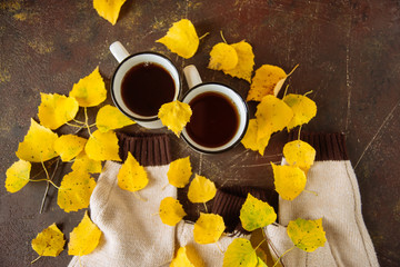 mugs surrounded by yellow foliage with a book and a knitted scarf, the concept of warmth and autumn sadness