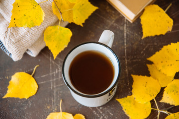 two white mugs surrounded by yellow leaves with a book and a knitted scarf, the concept of warmth and autumn sadness