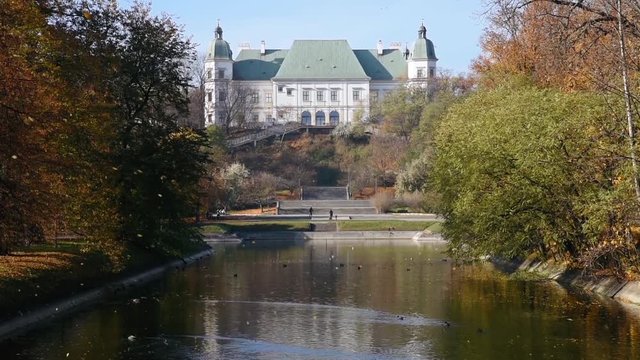 City park Royal Lazienki with pond or lake and  Ujazdowski Castle on background with blue sky, trees and fallen leaves at autumn. Warsaw, Poland, Europe. Camera move from bottom to top