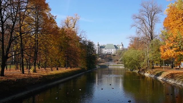 City park Royal Lazienki with pond or lake and  Ujazdowski Castle on background with blue sky, trees and fallen leaves at autumn. Warsaw, Poland, Europe. Camera move from left to right