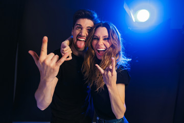 Loving couple having fun resting in a night disco club on concert showing rock gesture.