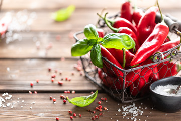 Red chili peppers with a sprig of basil in a wicker metal basket on a wooden background